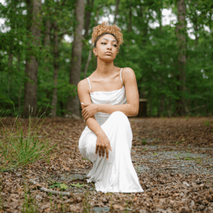 Cantfindcris in a white gown bending for a pose on leaves